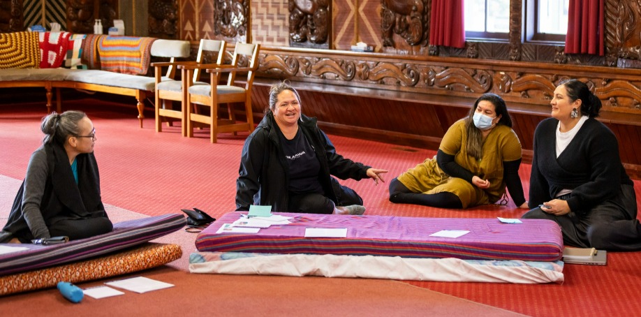 Four women are sitting talking in a marae
