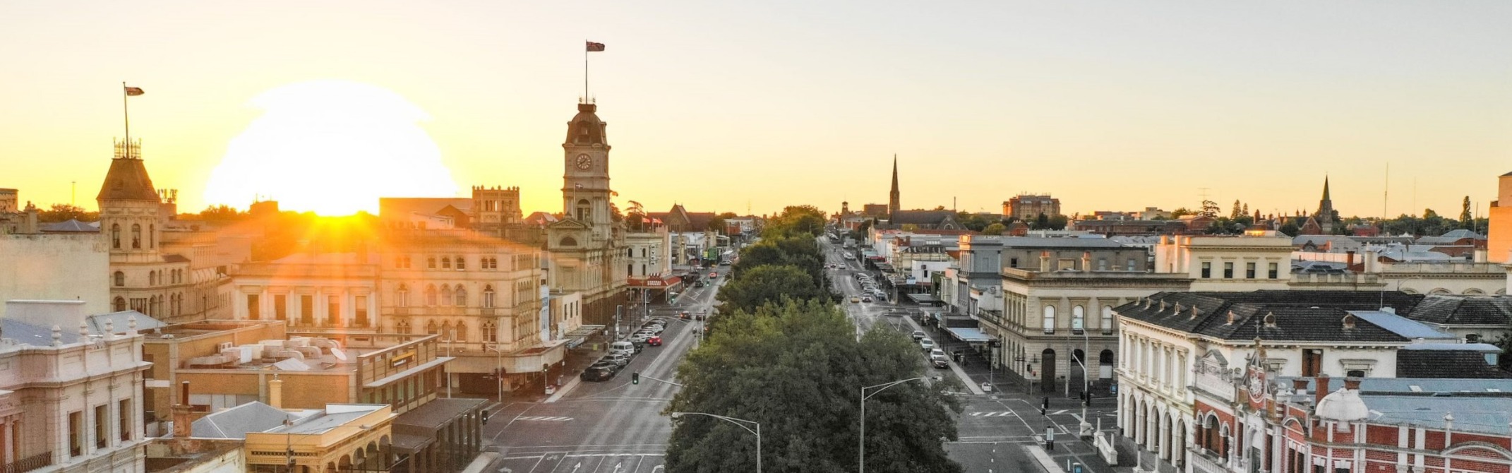 A city street in Ballarat at sunset, with buildings and cars creating a vibrant urban scene.