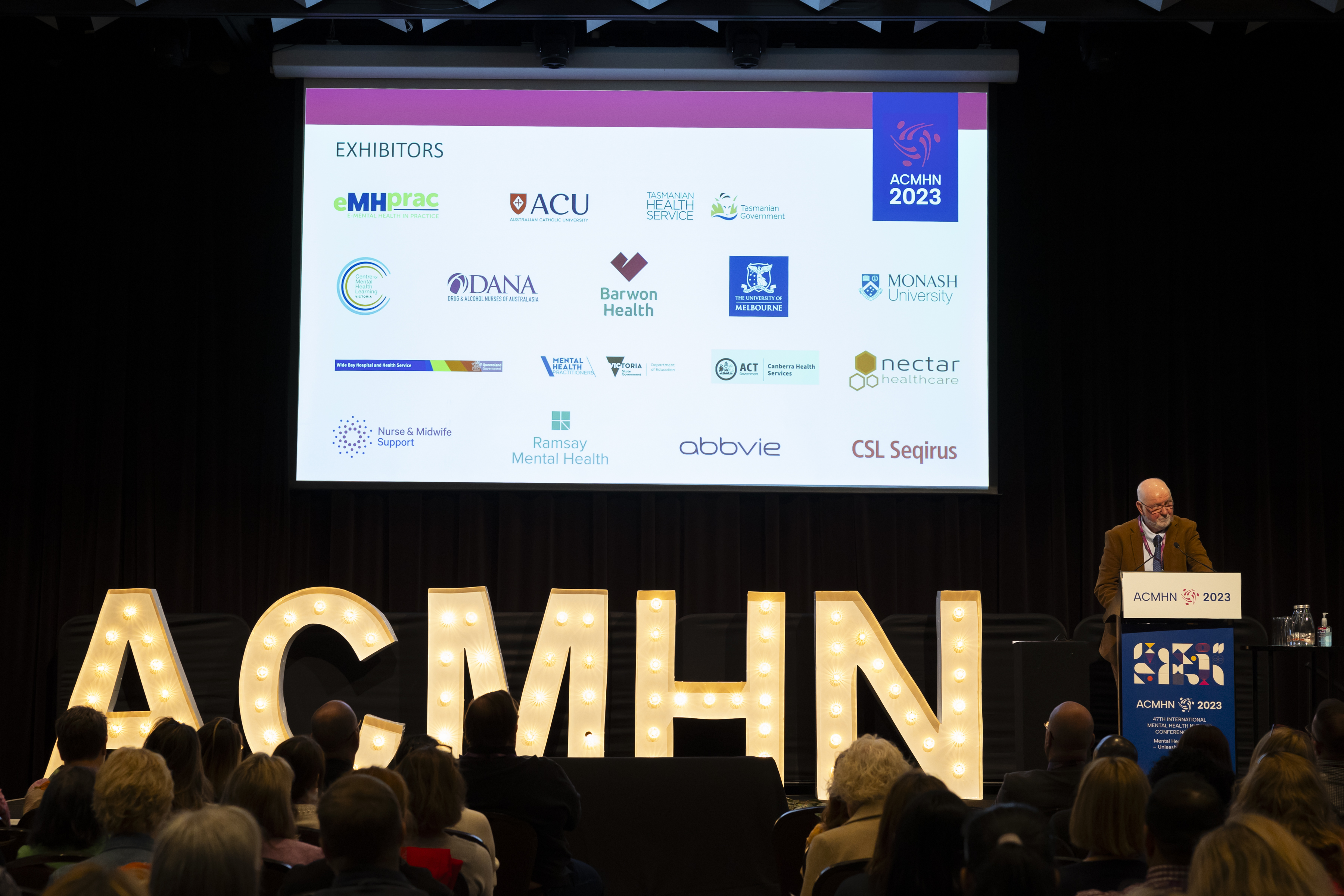 Speaker talking at a podium with ACMHN letters on stage.