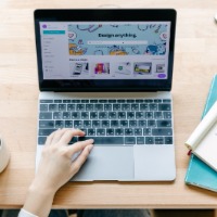 Photo of a laptop on a wood table with a person typing. 