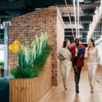 Photo of three women walking down a hallway with green plants. 