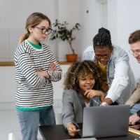 Photo of two women and two men standing behind a laptop. One of the men is pointing at the screen 